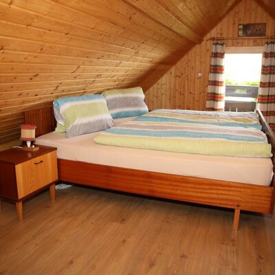 Attic double bedroom in the Farm House with wood paneling, a wooden bed, nightstand, built-in wardrobe, and access to a balcony.