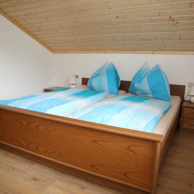 Double bedroom in the farmhouse featuring a wooden bed, two bedside tables with lamps, and a sloped wooden ceiling.