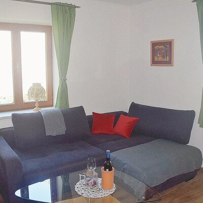The living area in the Farm House features an L-shaped sofa, a glass coffee table, and windows with light green curtains.