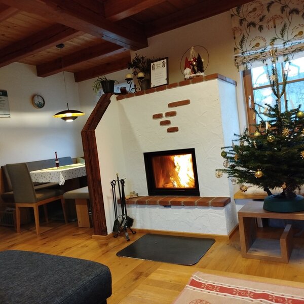 The farmhouse living area features a white plaster fireplace with exposed brick accents and a burning fire, a corner dining area, and wooden ceiling beams.