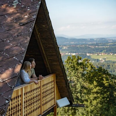 The farmhouse's inviting wooden balcony offers scenic, panoramic views of the surrounding green hills.