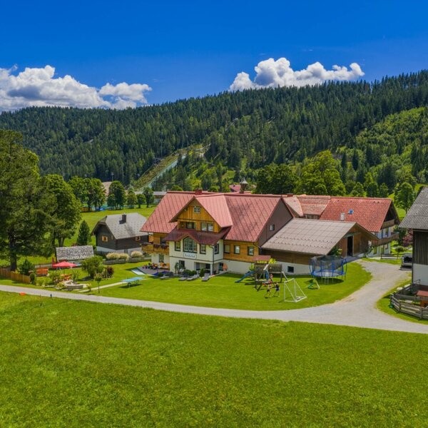 The farmhouse with a playground, trampoline, and swings, set against a mountain backdrop