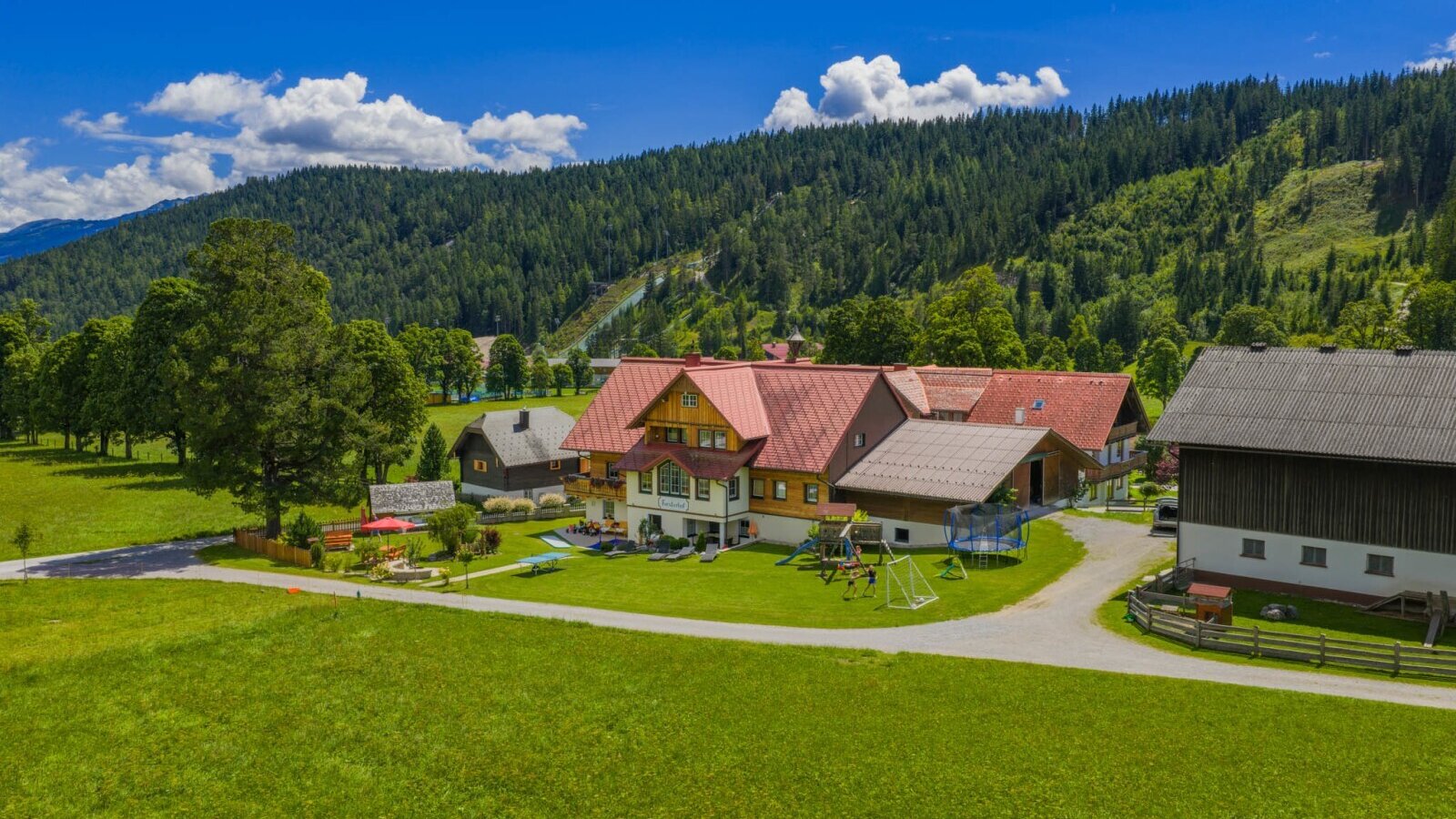 The farmhouse with a playground, trampoline, and swings, set against a mountain backdrop