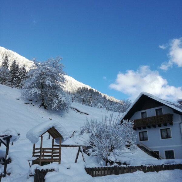 The farm house exterior with a snow-covered wooden swing set and mountainous winter landscape. The farm house exterior with a snow-covered wooden swing set and mountainous winter landscape.