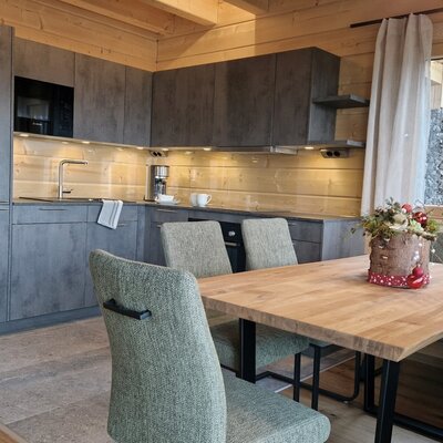 The farm house's fully equipped kitchen includes grey cabinetry and a coffee machine, alongside a dining area with a wooden table, chairs, and bench seating.