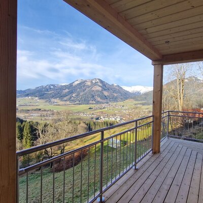 The farm house's balcony features a wooden deck and railing, offering views of the valley, village, and snow-capped mountains.