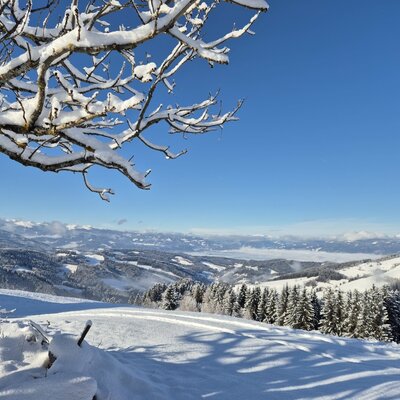 A winter view of snow-covered hills and distant mountains surrounding the farmhouse.