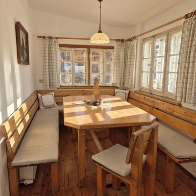 The dining area in the farmhouse features a wooden hexagonal table, corner bench seating with cushions, and wooden chairs.