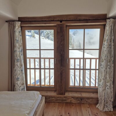 Farmhouse bedroom with a bed and windows overlooking snowy mountains.