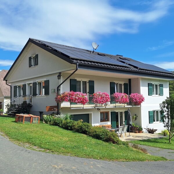 Exterior view of the farmhouse with a balcony, green shutters, and solar panels on the roof.