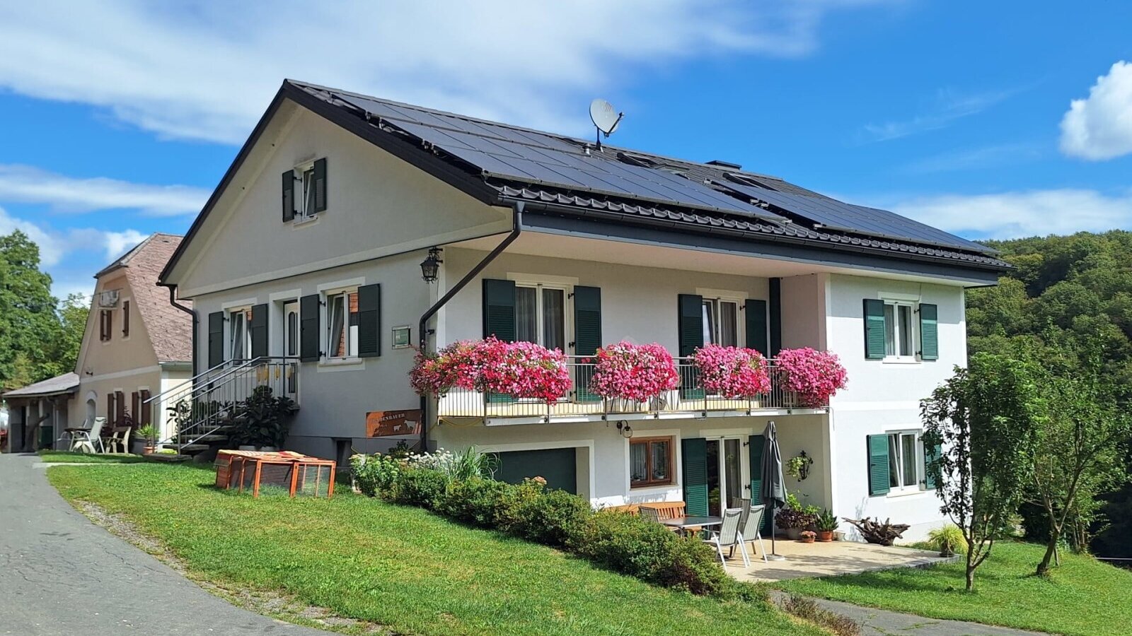 Exterior view of the farmhouse with a balcony, green shutters, and solar panels on the roof.