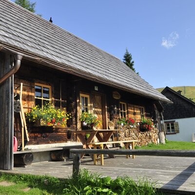 The farmhouse features a wooden shingle roof, flower boxes under its windows, and a front deck with a picnic table.