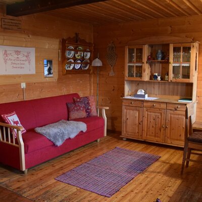 The farmhouse living space offers a red sofa, a traditional wooden cabinet, and a dining area.