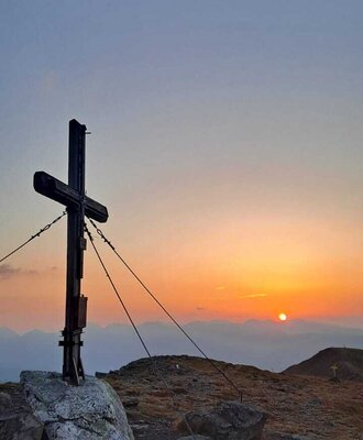 A mountain summit cross on a peak at sunset, representative of the alpine hiking experiences available to guests of the farmhouse.