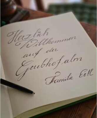 The farmhouse's guestbook featuring a handwritten "Herzlich Willkommen auf der Grubhofalm" message.
