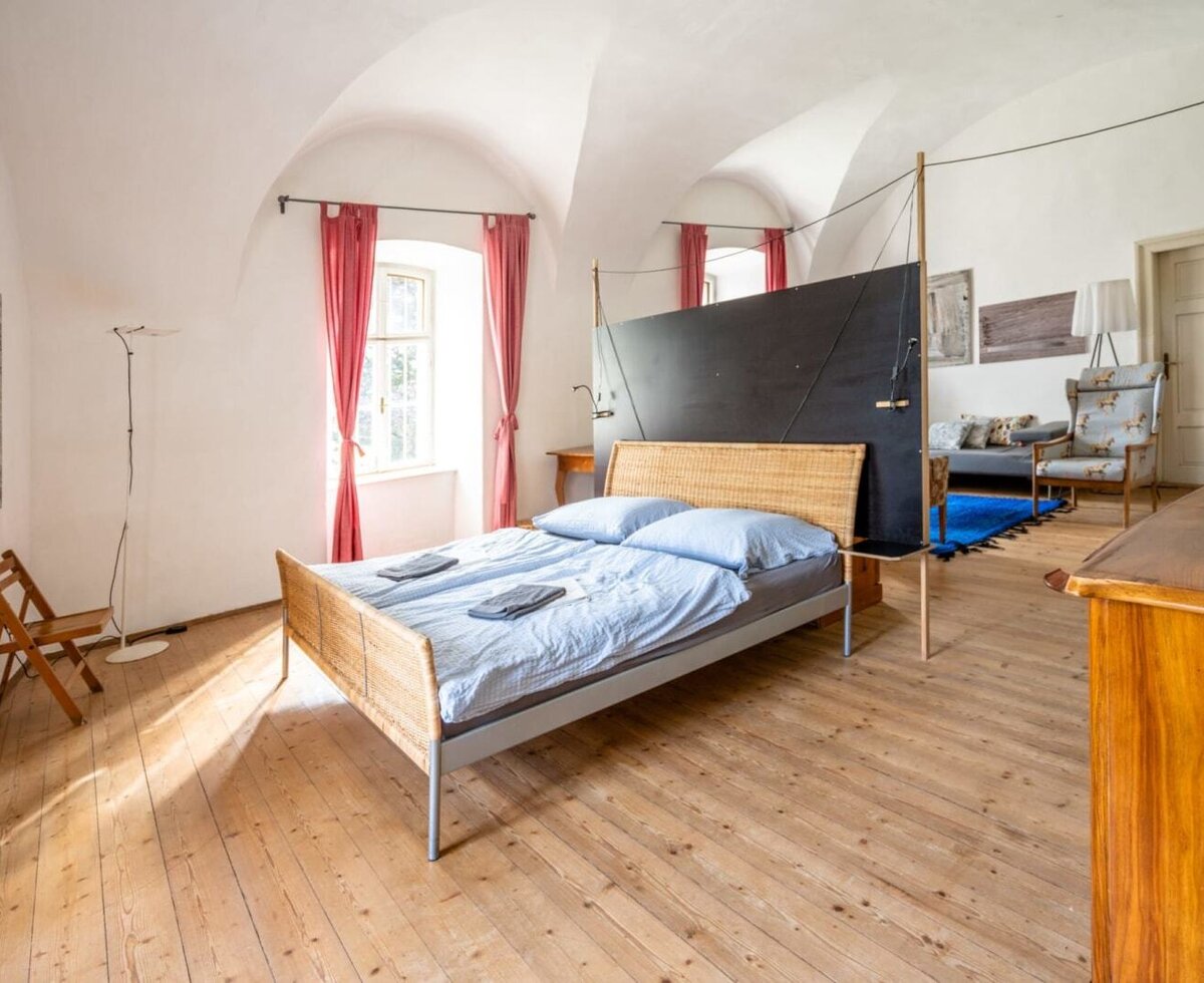 A spacious bedroom featuring high vaulted ceilings, wooden floors, an inviting double bed, and an adjacent living area.