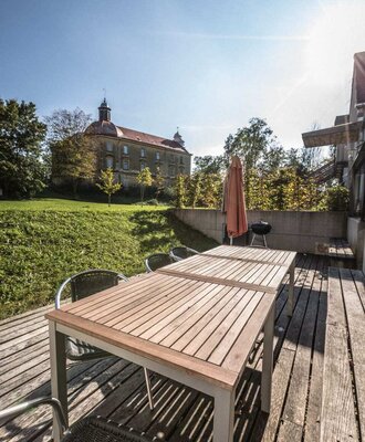 Inviting wooden terrace features a spacious outdoor dining table and views of the historic building nearby.