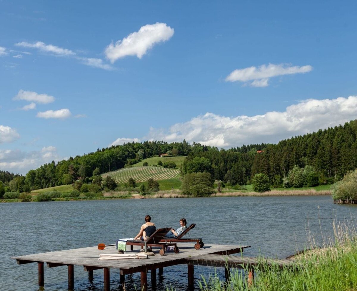 An idyllic wooden jetty by the farmhouse's lake, featuring comfortable sun loungers and scenic views of the surrounding green hills.
