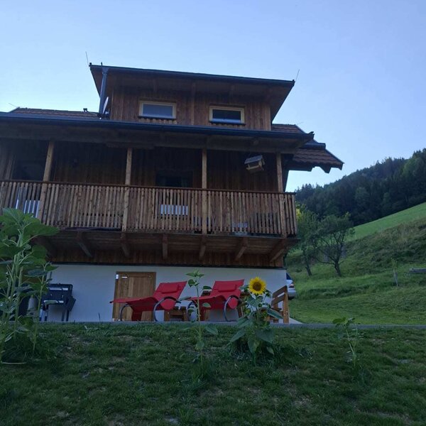 The inviting wooden bed and breakfast featuring comfortable red lounge chairs on the lawn against a scenic green hillside.