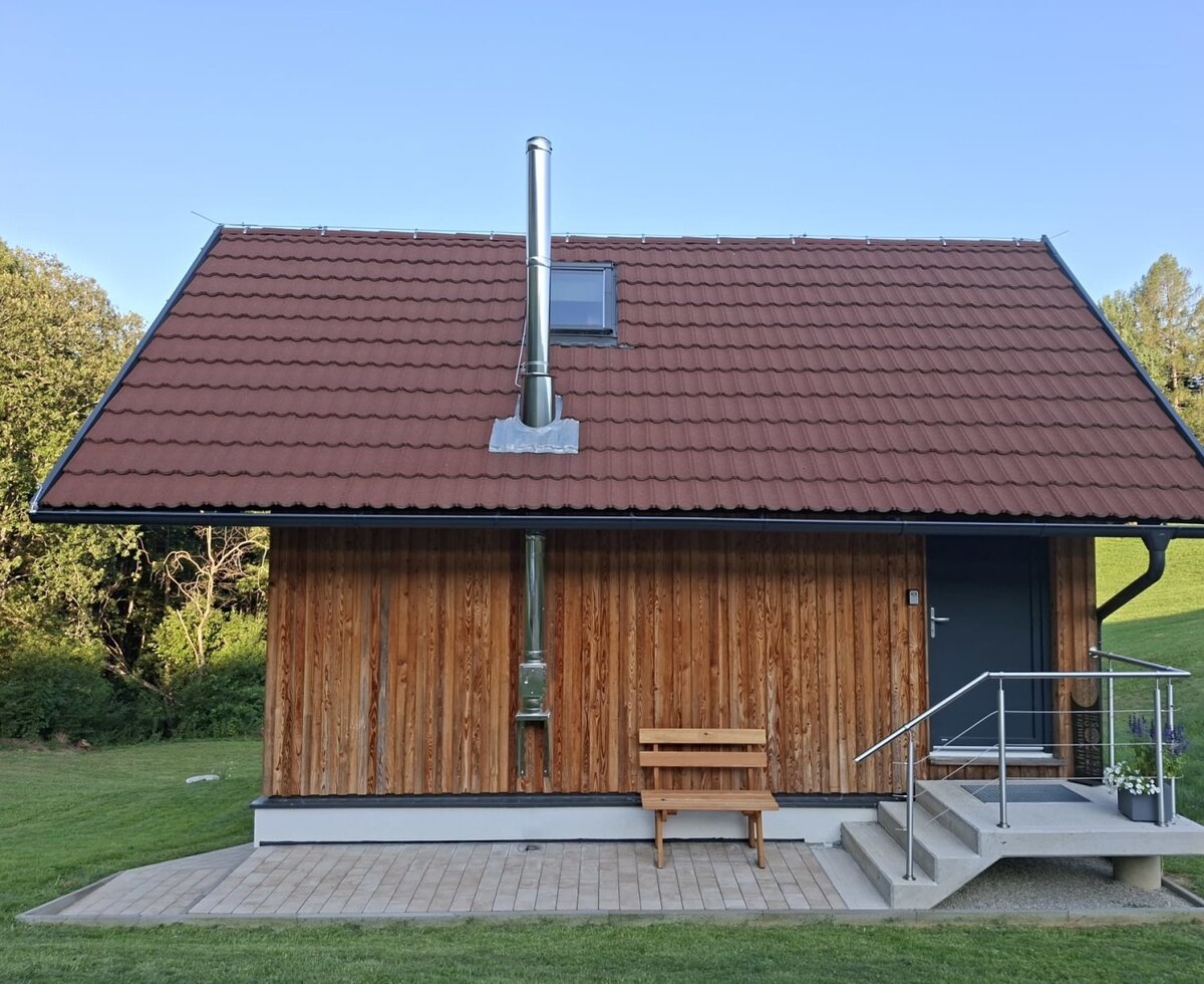 The charming exterior of the bed and breakfast, featuring warm wood cladding, a cozy wooden bench, and an inviting green lawn.