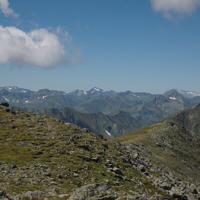 The mountainous landscape surrounding the farmhouse, featuring rocky terrain and distant peaks with patches of snow.