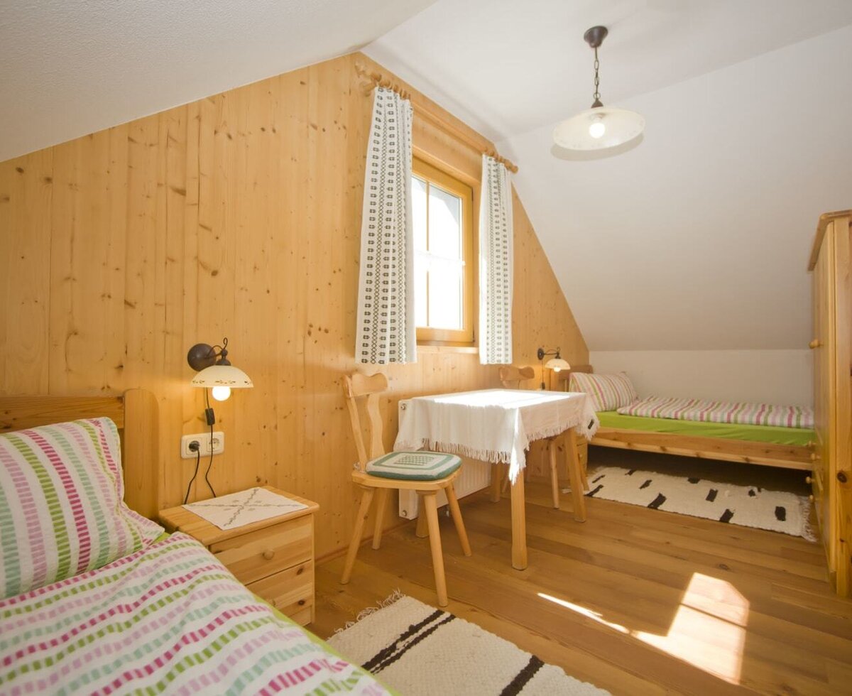 Bedroom in the farmhouse with two single beds, a small table with two chairs, a window, and a wooden wardrobe.