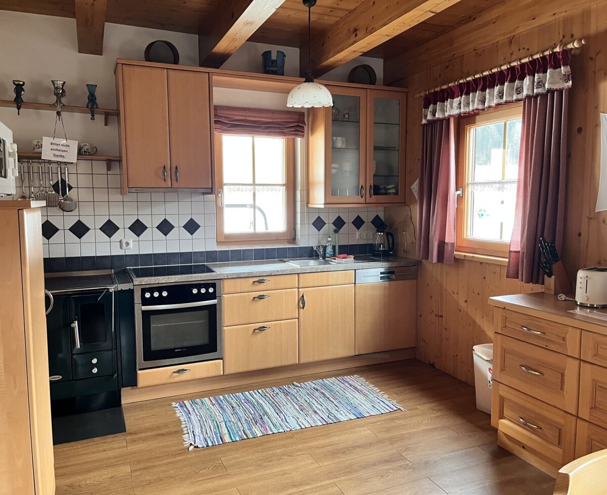 Fully equipped wooden kitchen in the Almhütte with a sink, electric hob, oven, and a traditional wood-burning stove.