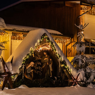 Illuminated nativity scene in the snow, complemented by strings of lights.