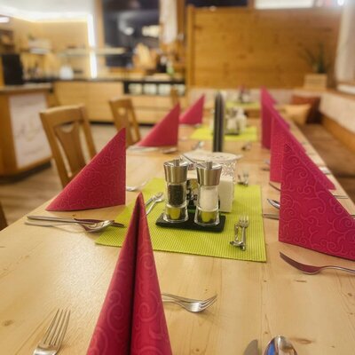The dining area of the farmhouse, featuring a long wooden table set with red napkins and cutlery, and a buffet in the background.