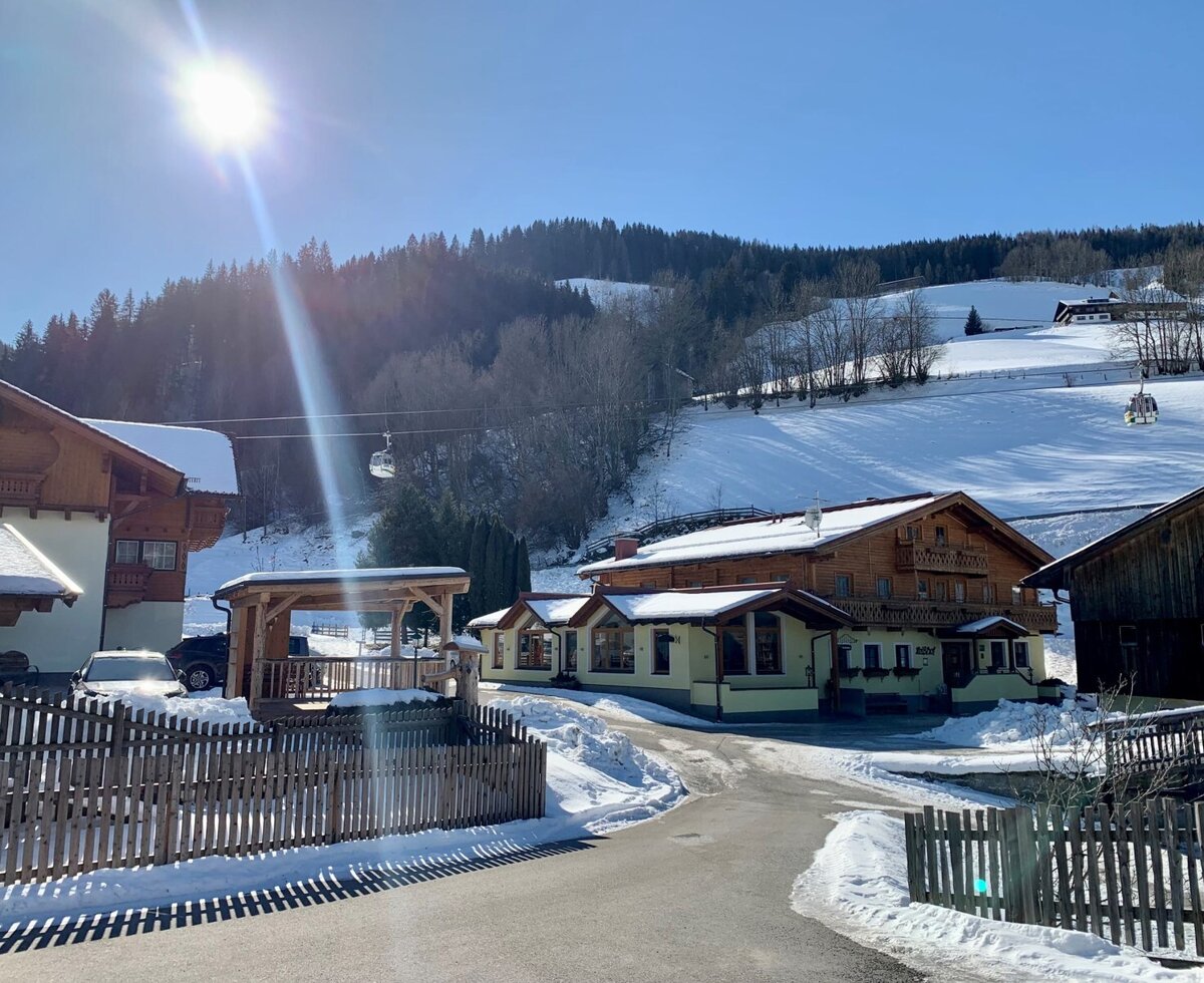 Exterior view of the farmhouse in winter, surrounded by snowy mountains and a visible ski lift.