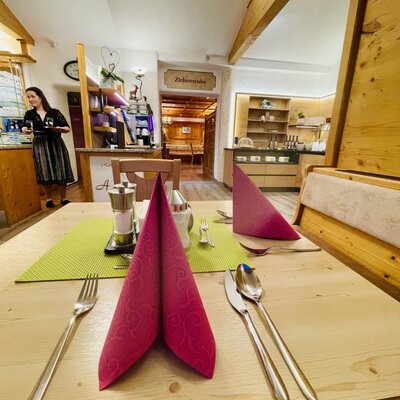 A set table in the dining area of the farmhouse, with cutlery and napkins, showing a buffet and service staff in the background.