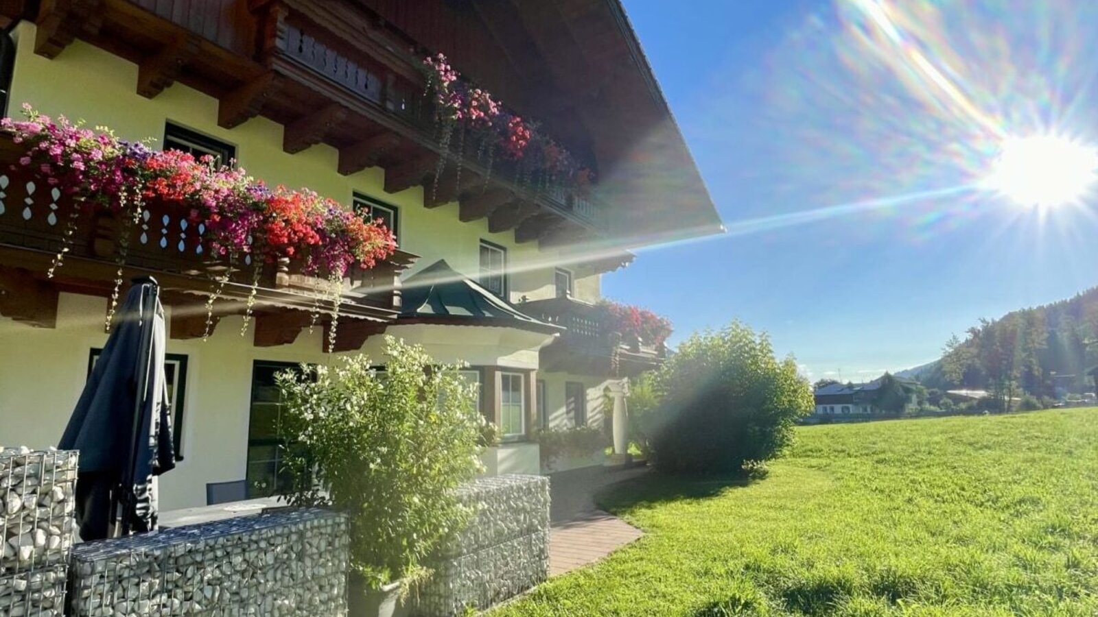 Exterior view of the farmhouse with flower-decorated balconies and an adjacent green meadow.