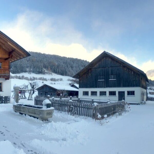 The snow-covered exterior of the farmhouse with its buildings and the winter mountain landscape.