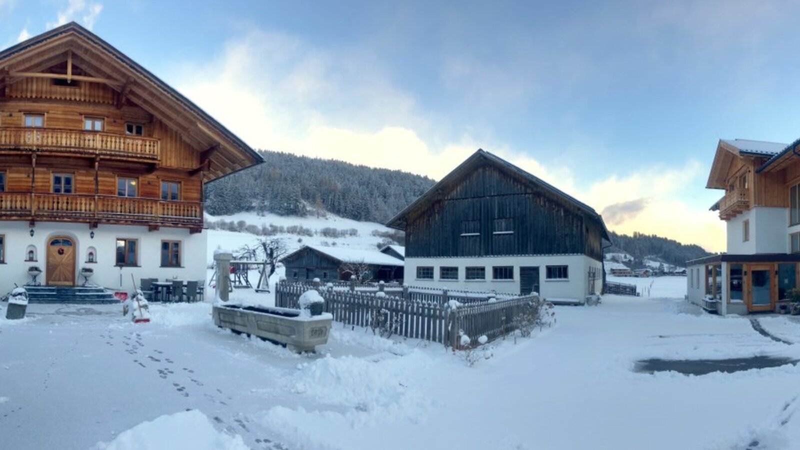 The snow-covered exterior of the farmhouse with its buildings and the winter mountain landscape.