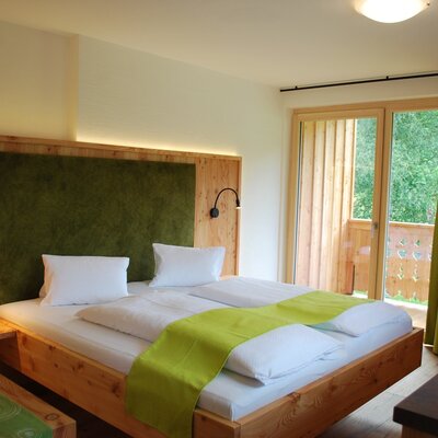 Double bedroom in the farmhouse with a wooden bed, green headboard, reading lamps, and balcony access.