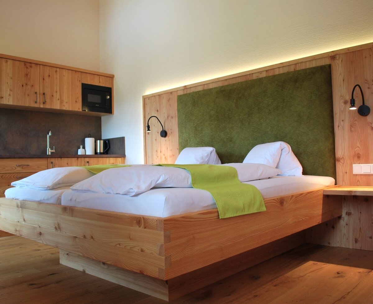 Spacious bedroom in the farmhouse with a double bed, green headboard, and an integrated kitchenette with a sink and microwave.