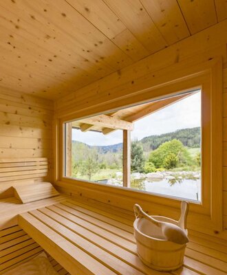 Sauna on the farm with wooden benches and a large window with a view of the landscape and a pond. copyright: ELISABETH FRÖHLICH photography