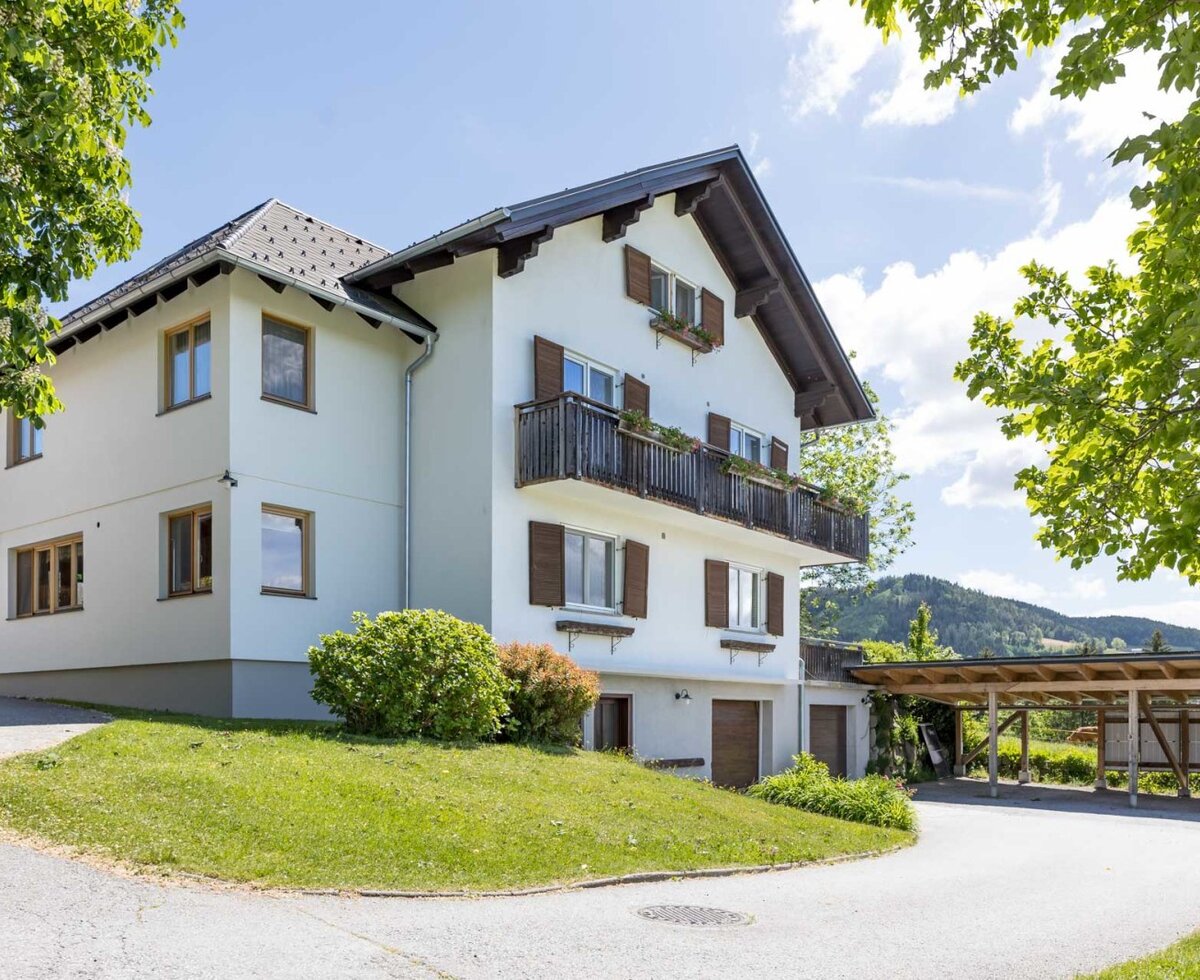 The farmhouse's inviting exterior with a well-kept green lawn and a spacious carport.