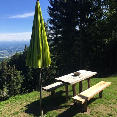 Wooden picnic table and benches with a closed umbrella on the farmhouse grounds, overlooking a valley view.