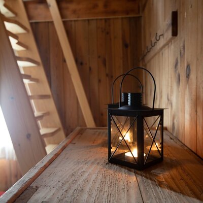 An illuminated lantern on a rustic wooden chest, set against wooden walls and a staircase within the farmhouse.