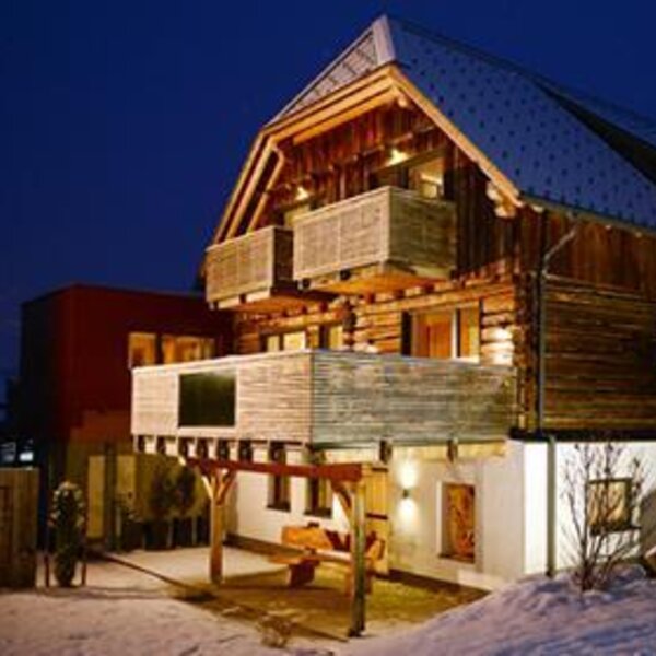 The exterior of the illuminated farm house at night, featuring wooden balconies and a snow-covered environment. The exterior of the illuminated farm house at night, featuring wooden balconies and a snow-covered environment.