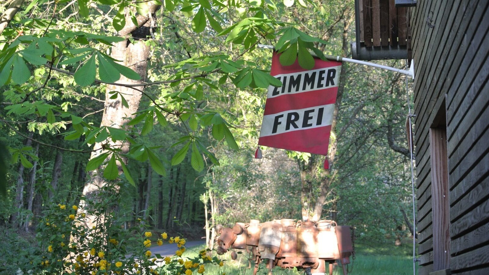 The 'ZIMMER FREI' (Rooms Available) sign at the farmhouse, surrounded by trees and old farm implements.