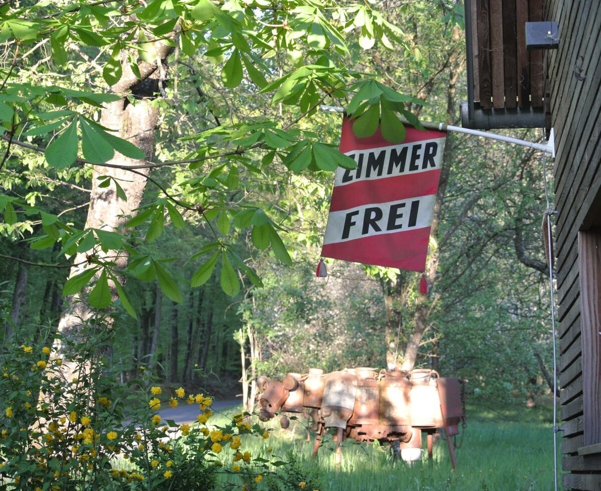 The 'ZIMMER FREI' (Rooms Available) sign at the farmhouse, surrounded by trees and old farm implements.
