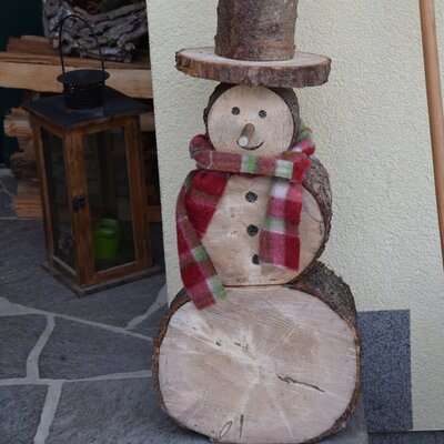 A decorative wooden snowman with a plaid scarf stands on the stone steps of the farmhouse.