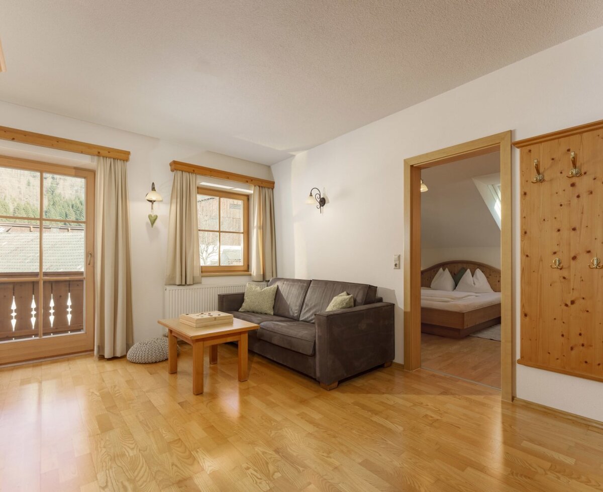Living area of the farmhouse with a sofa, coffee table, wooden floor, handcrafted wooden cabinet, and balcony access, with a view into the bedroom.