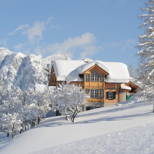 The Farm House exterior in a winter setting, with snow covering the roof, surrounding trees, and mountains.