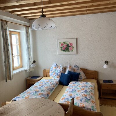 Bedroom in the farm house with two single beds, a wooden ceiling, and a seating area with a round wooden table.