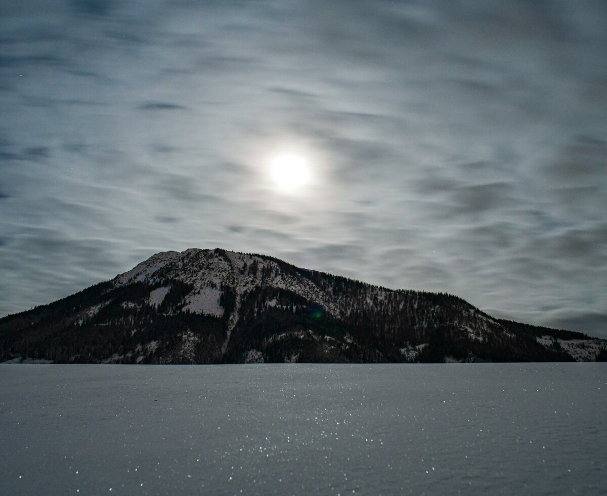 Atmospheric view from the farmhouse of the snow-covered mountain landscape under a cloudy, moonlit sky.
