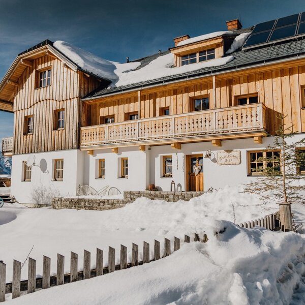 The farm house exterior features traditional wooden balconies, solar panels, and is surrounded by snow in a mountain setting. The farm house exterior features traditional wooden balconies, solar panels, and is surrounded by snow in a mountain setting.
