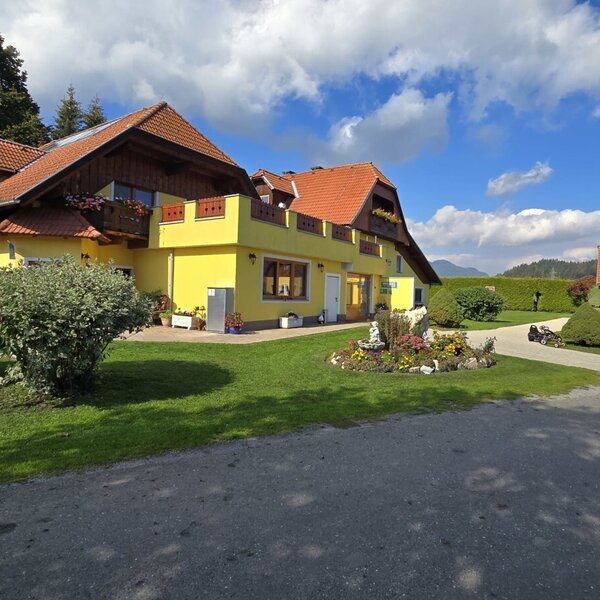 The inviting exterior of the farmhouse, featuring a well-kept garden and a spacious green lawn under a blue sky.